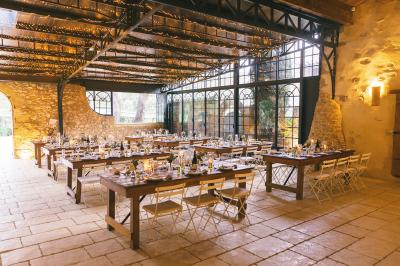 Table dressée avec nappes blanches, verres à vin, couverts, petits pains et centre de table floral dans une salle lumineuse.