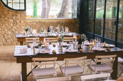 Table dressée avec nappes blanches, verres à vin, couverts, petits pains et centre de table floral dans une salle lumineuse.