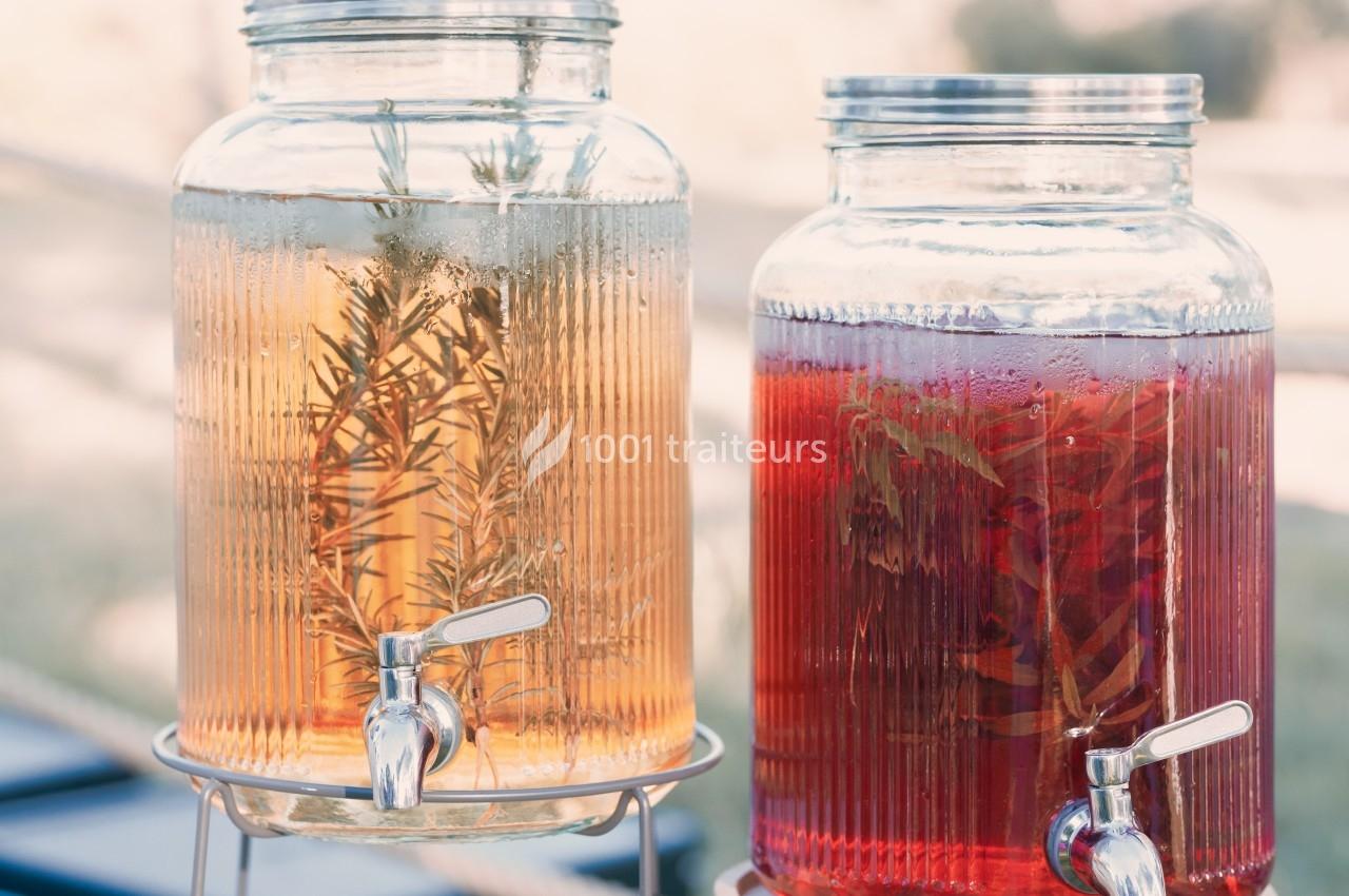 Deux distributeurs en verre contenant des boissons infusées, l'un avec du romarin, l'autre avec des herbes rouges.