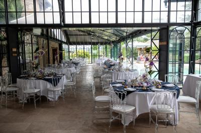 Table dressée avec nappes blanches, verres à vin, couverts, petits pains et centre de table floral dans une salle lumineuse.