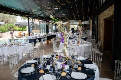 Table dressée avec nappes blanches, verres à vin, couverts, petits pains et centre de table floral dans une salle lumineuse.