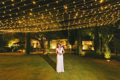 Table dressée avec nappes blanches, verres à vin, couverts, petits pains et centre de table floral dans une salle lumineuse.