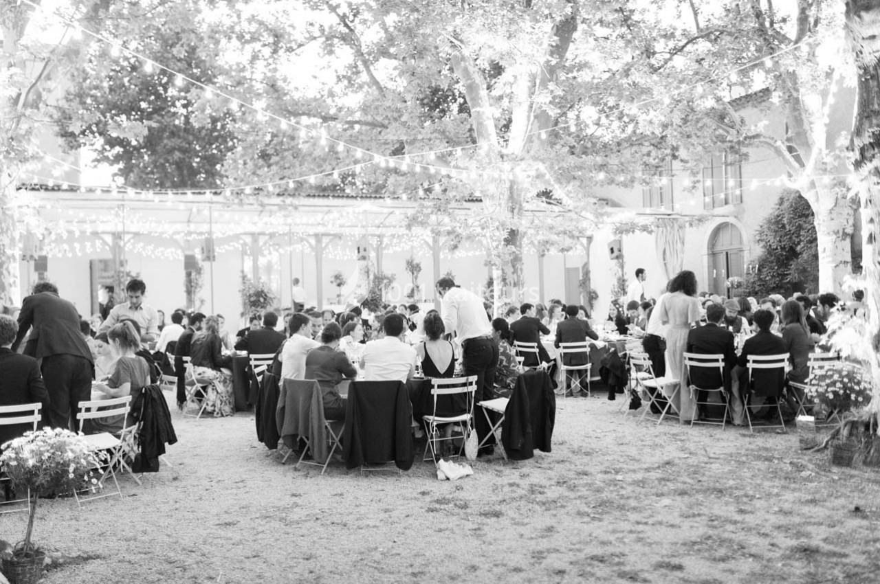 Groupe de personnes assises à des tables en extérieur, sous des guirlandes lumineuses, lors d'un événement festif.