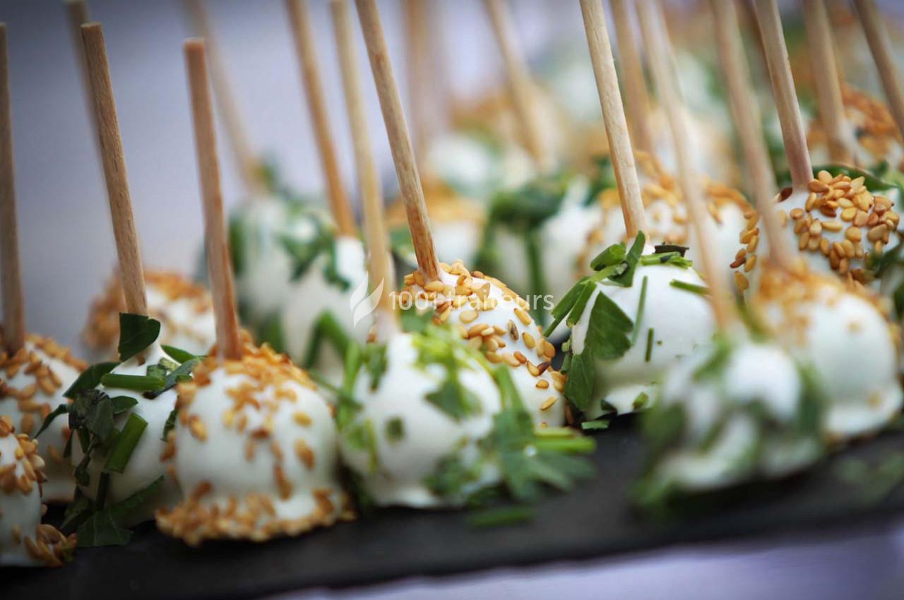 Boules apéritives enrobées de fromage, garnies de graines de sésame et d'herbes fraîches, présentées sur des bâtonnets.