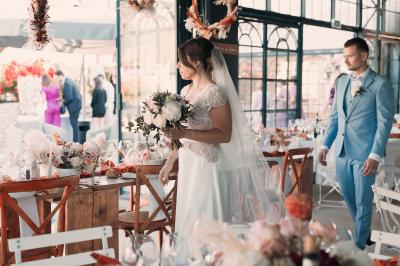 Miniature Traiteur Aix-en-Provence (Bouches-du-Rhône) - Carré Gourmand #38 Une mariée en robe blanche tient un bouquet dans une salle décorée pour un mariage, avec un homme en costume bleu derrière…