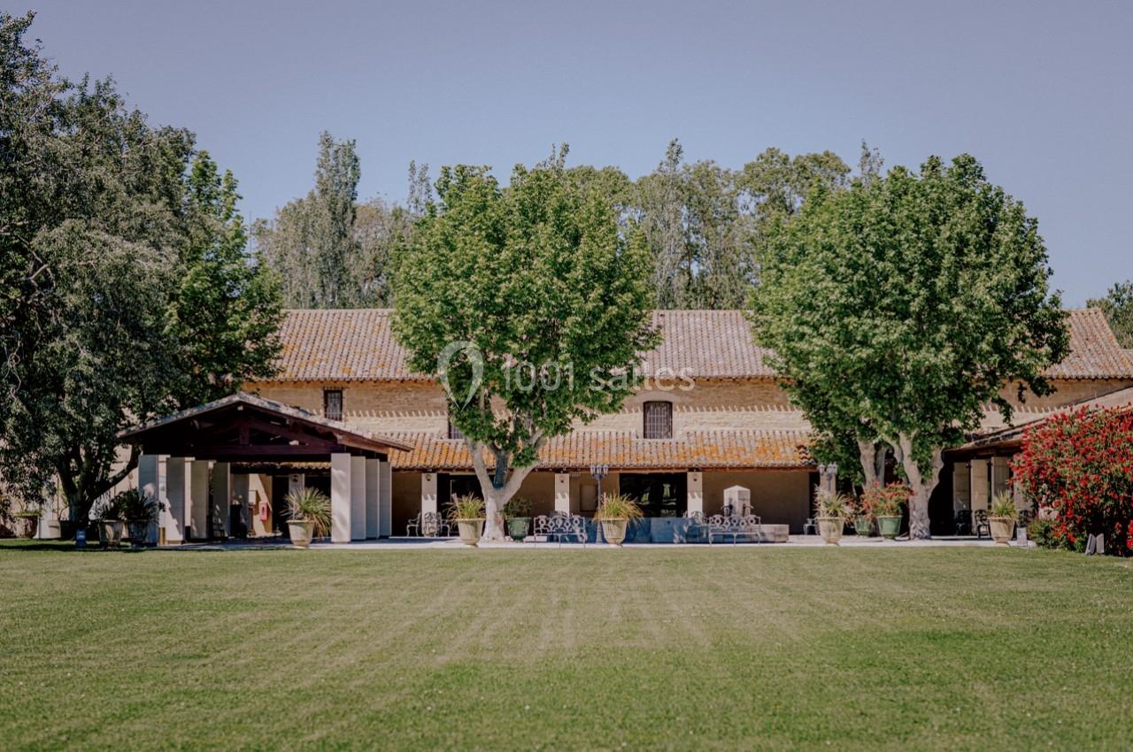 Bâtisse en pierre avec toit en tuiles, entourée d'arbres, pelouse bien entretenue au premier plan.