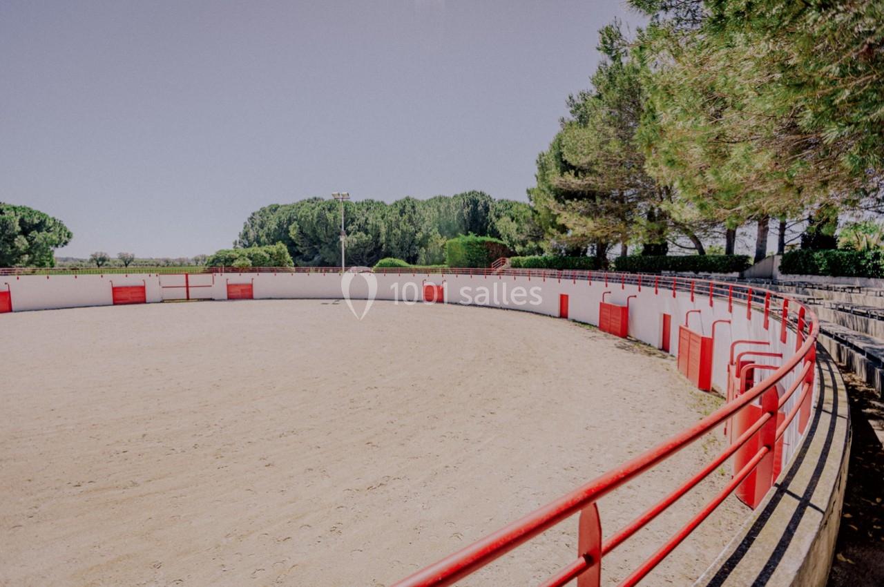 Arène circulaire en plein air avec barrières rouges, entourée d'arbres et d'un ciel dégagé.