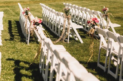Une mariée souriante brandit un éventail devant un gâteau de mariage décoré, entourée d'invités en extérieur.