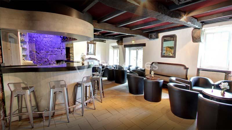 Intérieur d'un bar avec comptoir arrondi, tabourets métalliques, fauteuils noirs et murs en pierre apparente.