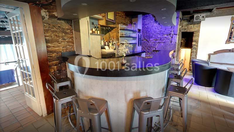 Bar en pierre avec comptoir incurvé, tabourets métalliques, étagères à bouteilles et éclairage tamisé.