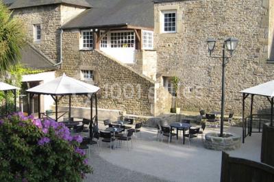 Terrasse extérieure avec tables et chaises en plastique sous une pergola, entourée de murs couverts de végétation.