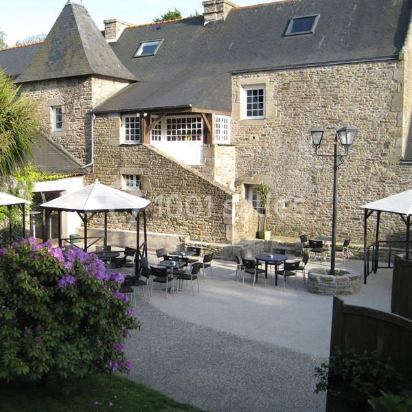 Cour extérieure d'une bâtisse en pierre avec terrasses aménagées, parasols et mobilier de jardin.