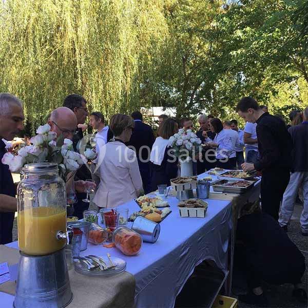 Personnes rassemblées autour d'une table en extérieur, avec buffet de nourriture et boissons sous des arbres.