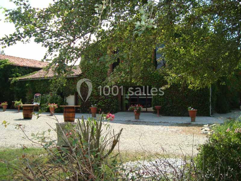 Bâtiment couvert de lierre entouré de pots de fleurs, avec une allée en gravier et des arbres en premier plan.