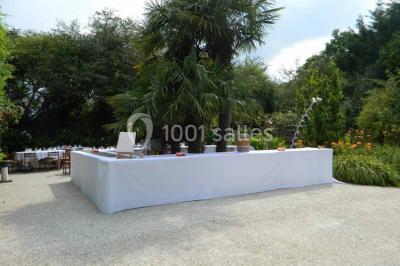 Chemin bordé d'arbres menant à un kiosque en bois avec un toit en tuiles, entouré de verdure.