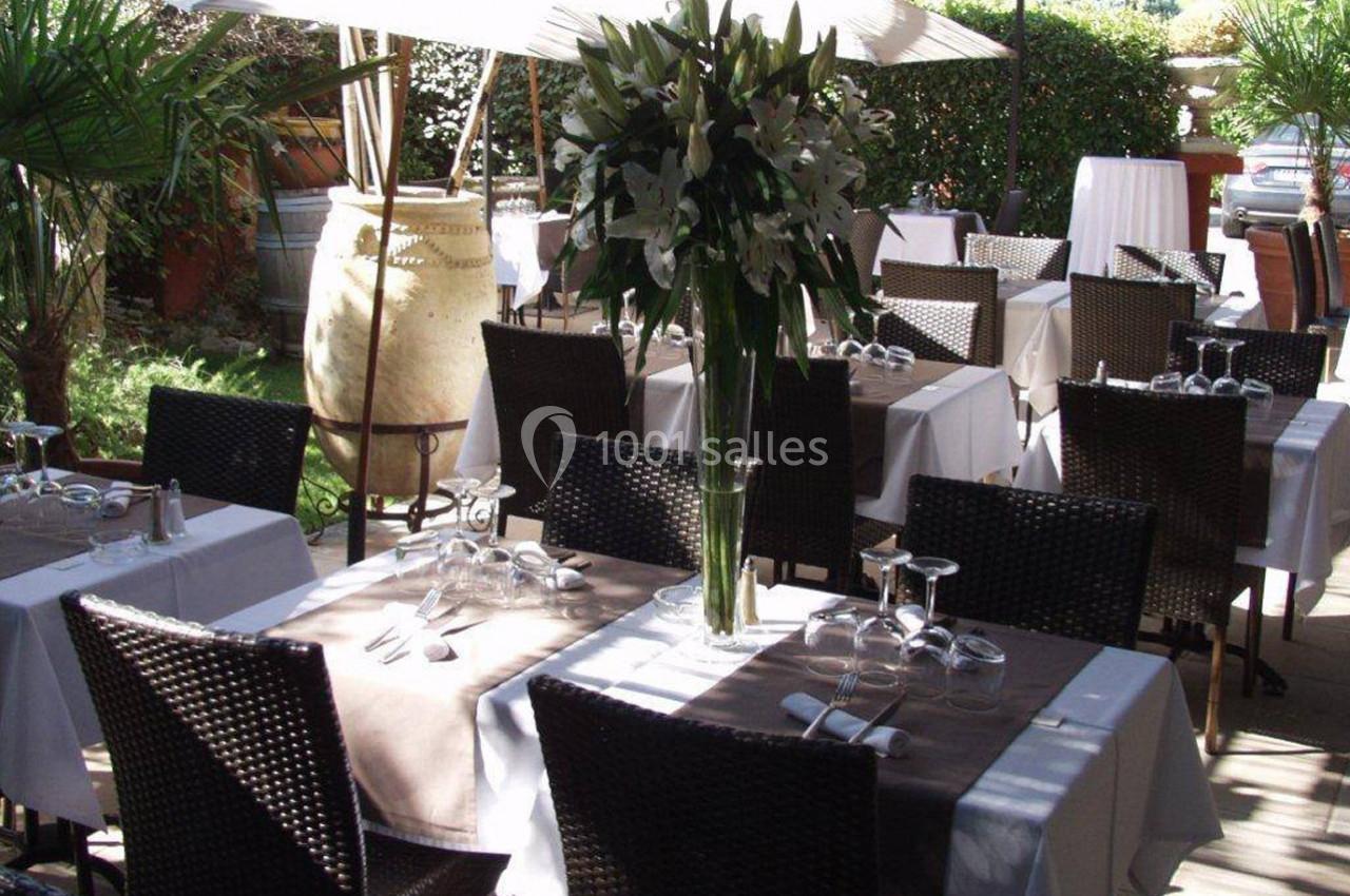 Terrasse d'un restaurant avec des tables dressées, nappes blanches, chaises en osier et décoration florale.