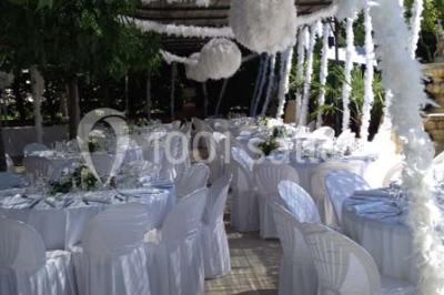 Table décorée avec une nappe blanche et rose, ornée de fleurs violettes et de plumes blanches, dans une salle festive.