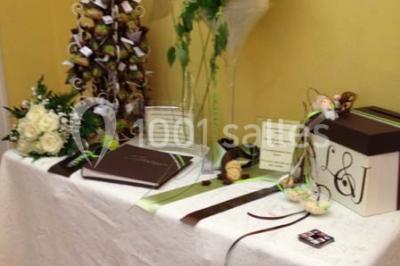 Table décorée avec une nappe blanche et rose, ornée de fleurs violettes et de plumes blanches, dans une salle festive.