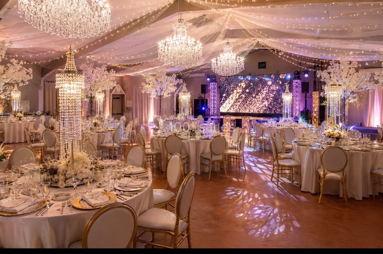 Salle de réception élégante décorée de chandeliers, guirlandes lumineuses et tables dressées pour un événement.