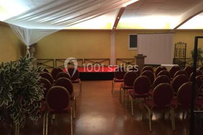 Salle de réception spacieuse avec tables hautes, chaises alignées, plantes décoratives et lustres suspendus.