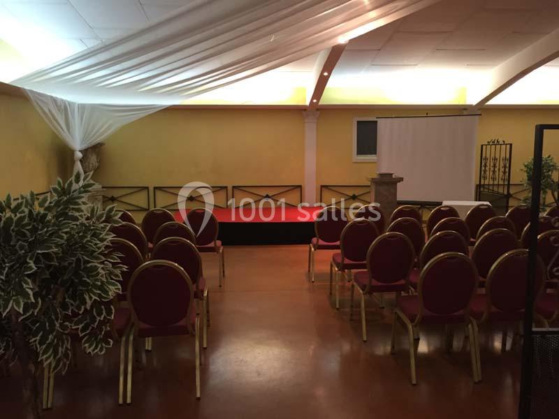 Salle de conférence avec chaises rouges alignées, scène surélevée, écran de projection et décoration sobre.