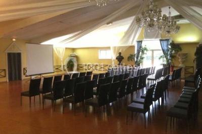 Salle de réception spacieuse avec tables hautes, chaises alignées, plantes décoratives et lustres suspendus.