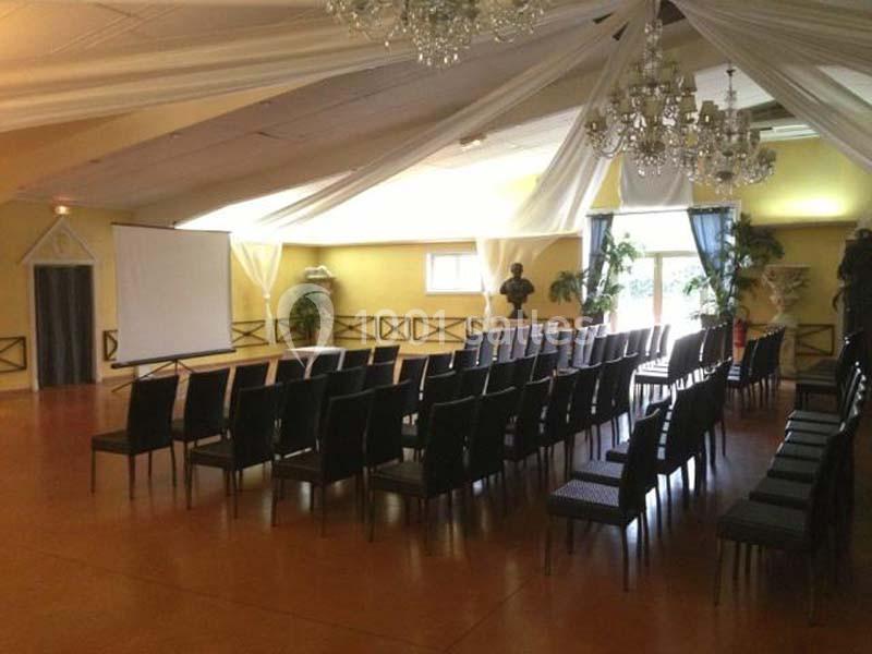 Salle de conférence avec des rangées de chaises noires, un écran de projection et des décorations élégantes.