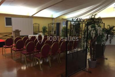 Salle de réception spacieuse avec tables hautes, chaises alignées, plantes décoratives et lustres suspendus.