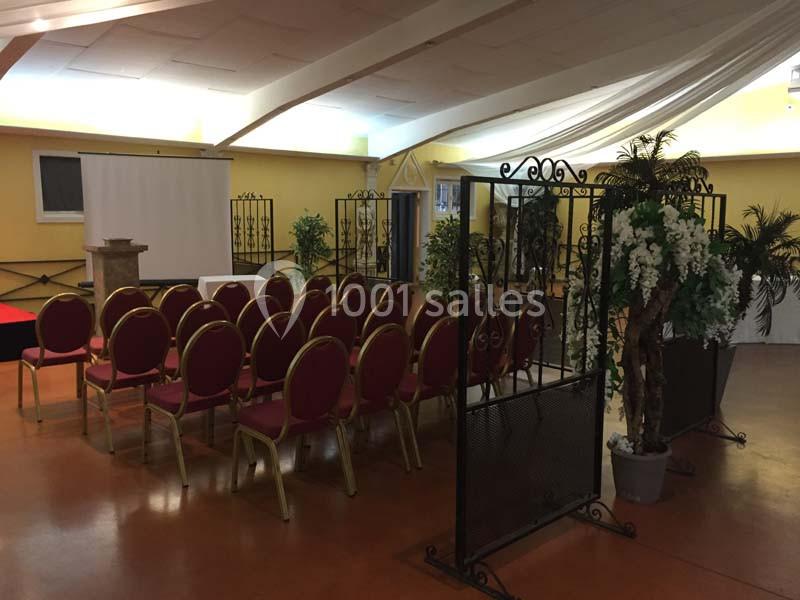 Salle aménagée avec des chaises rouges alignées face à un écran de projection, entourée de plantes décoratives.
