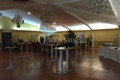 Salle de réception spacieuse avec tables hautes, chaises alignées, plantes décoratives et lustres suspendus.