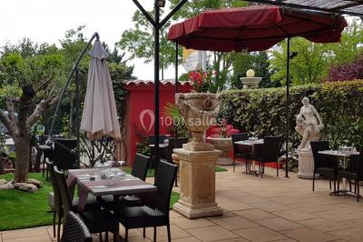 Salle de réception spacieuse avec tables hautes, chaises alignées, plantes décoratives et lustres suspendus.