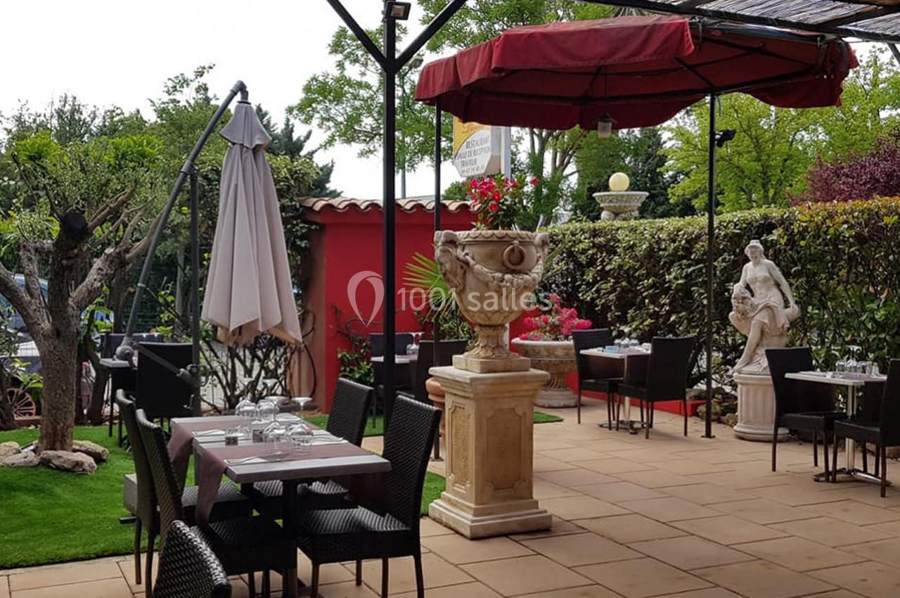 Terrasse extérieure avec tables dressées, parasols, statue décorative et végétation environnante.
