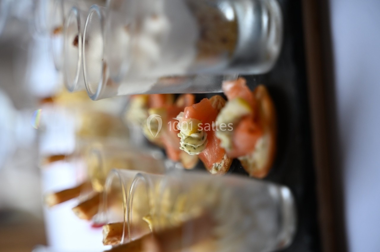 Assortiment de verrines et canapés garnis de saumon et crème, disposés sur un plateau noir.