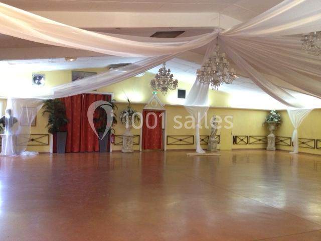 Salle de réception spacieuse avec sol en parquet, rideaux rouges, statues décoratives et plafonds ornés de drapés blancs.