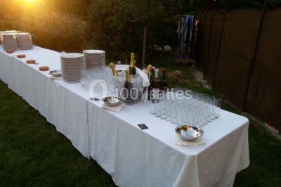 Salle de réception spacieuse avec tables hautes, chaises alignées, plantes décoratives et lustres suspendus.