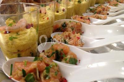 Salle de réception spacieuse avec tables hautes, chaises alignées, plantes décoratives et lustres suspendus.