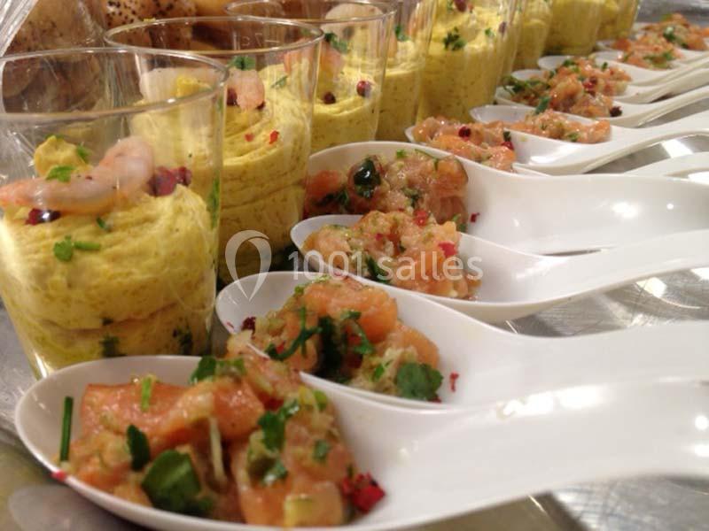 Verrines de mousse jaune et cuillères de tartare de saumon garnies de fines herbes, présentées sur une table.