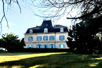 Manoir ancien entouré d'arbres, avec une pelouse en premier plan et un ciel clair en arrière-plan.