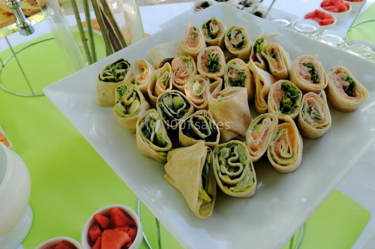 Plateau de wraps garnis de saumon, jambon et légumes, disposés sur une table avec des accompagnements.
