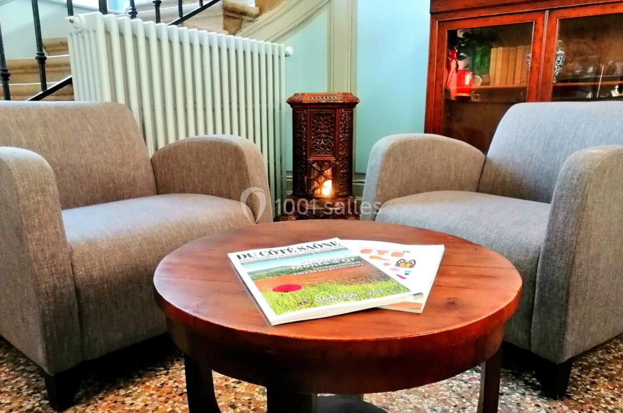 Deux fauteuils gris entourent une table ronde en bois avec des magazines, dans un salon au décor chaleureux.