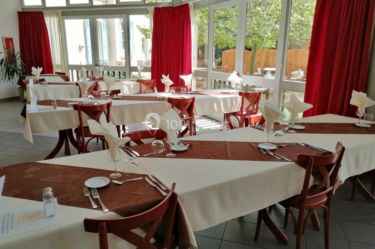 Salle de restaurant lumineuse avec tables dressées, nappes blanches et marron, et grandes baies vitrées donnant sur l…