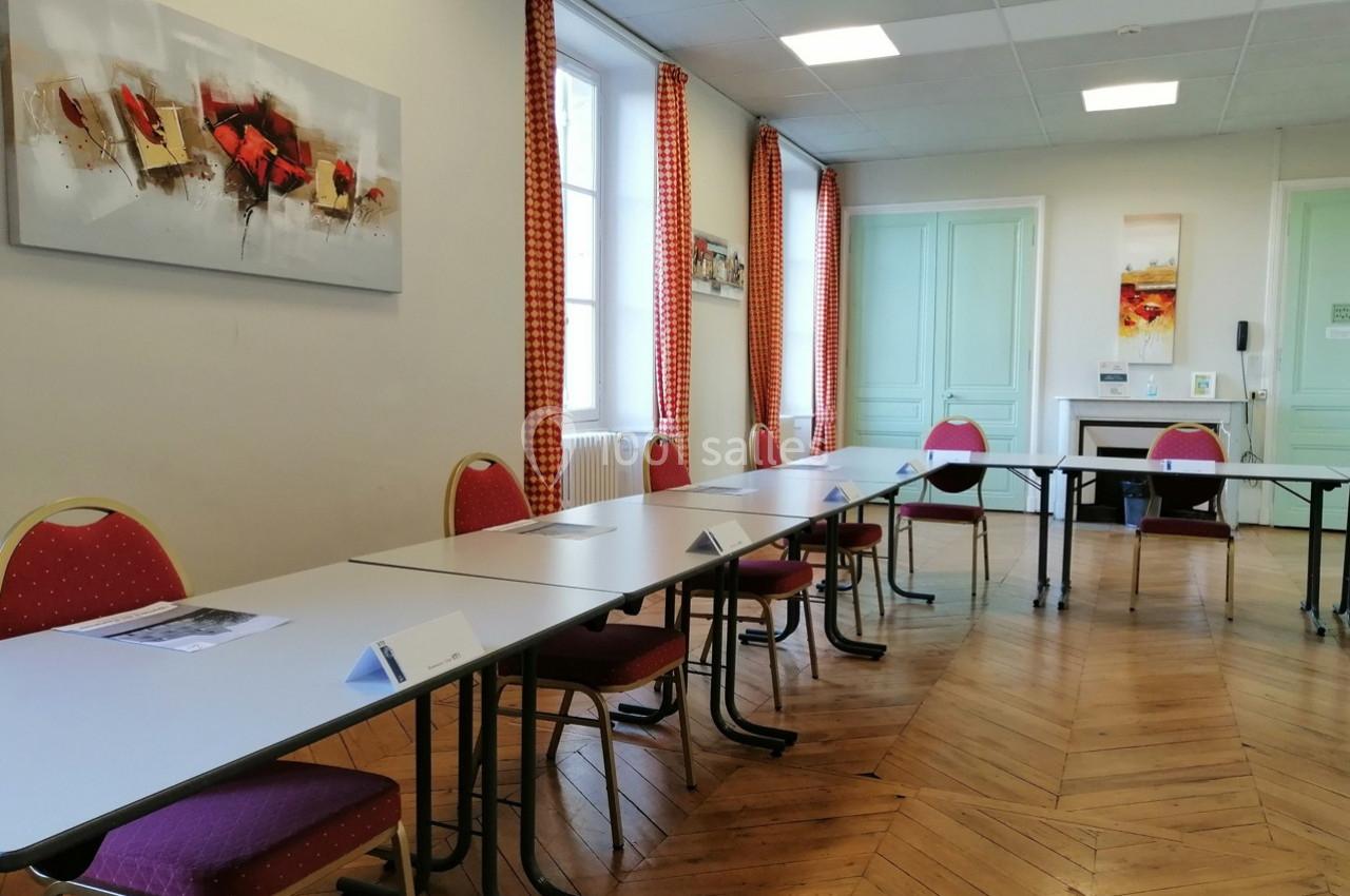 Salle de réunion lumineuse avec tables disposées en U, chaises rouges, parquet en bois et tableaux décoratifs au mur.