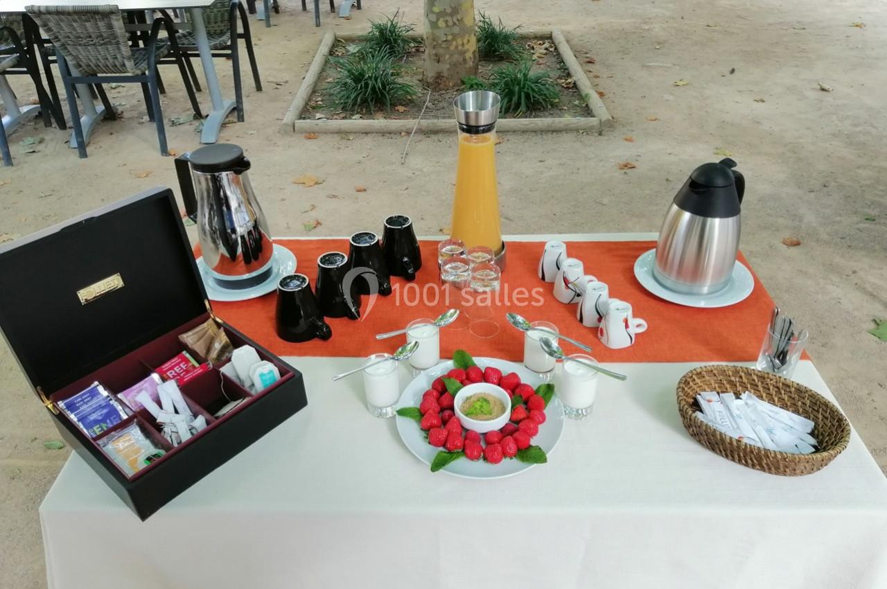 Table dressée en extérieur avec boissons chaudes, jus d'orange, fraises, condiments et accessoires de service.