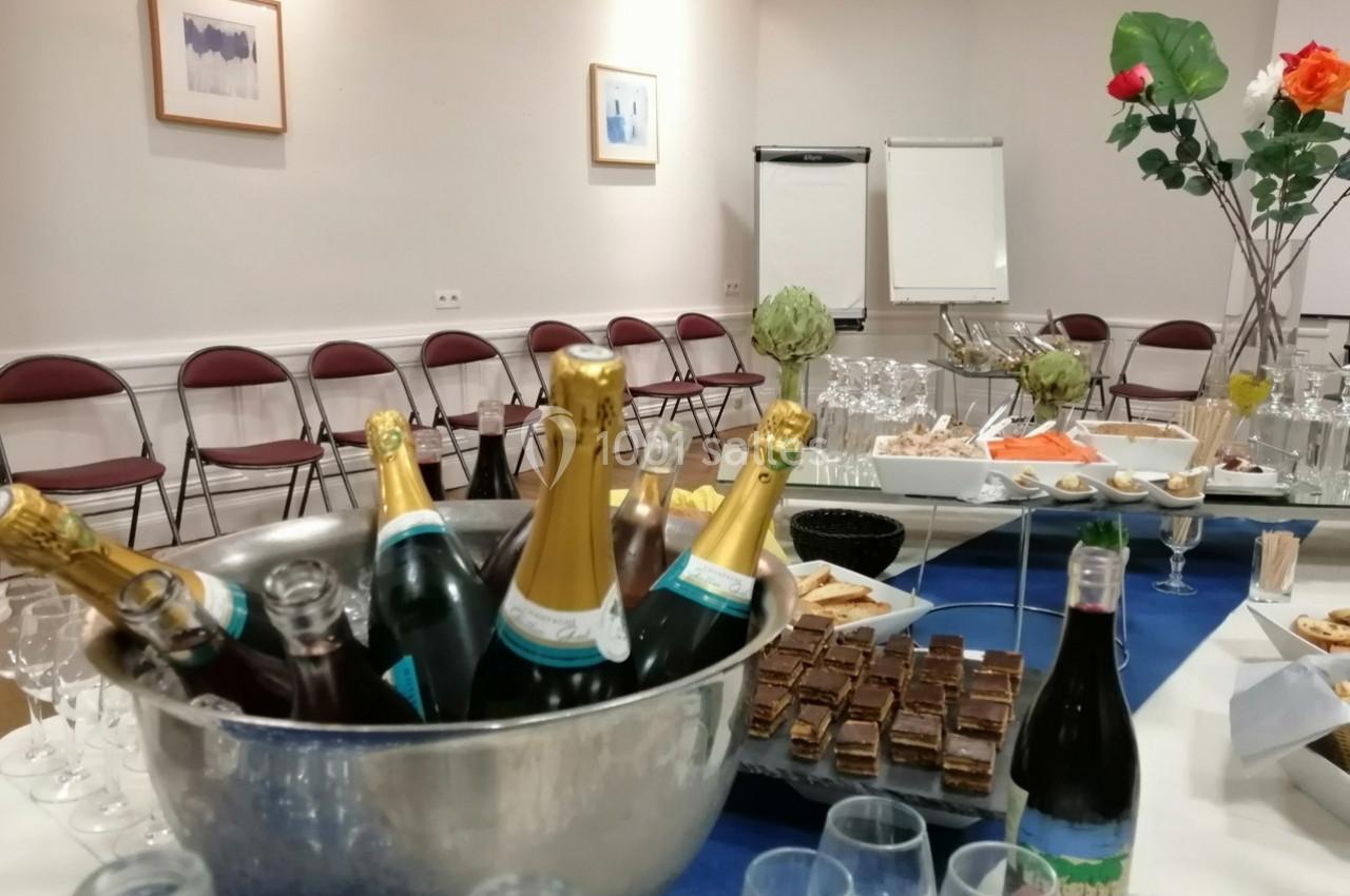 Table dressée pour un buffet avec bouteilles de champagne, verrines, desserts et chaises alignées en arrière-plan.