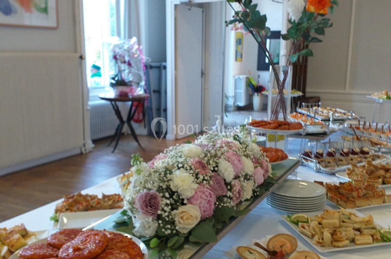 Buffet avec plats variés, fleurs décoratives au centre et salle lumineuse en arrière-plan.