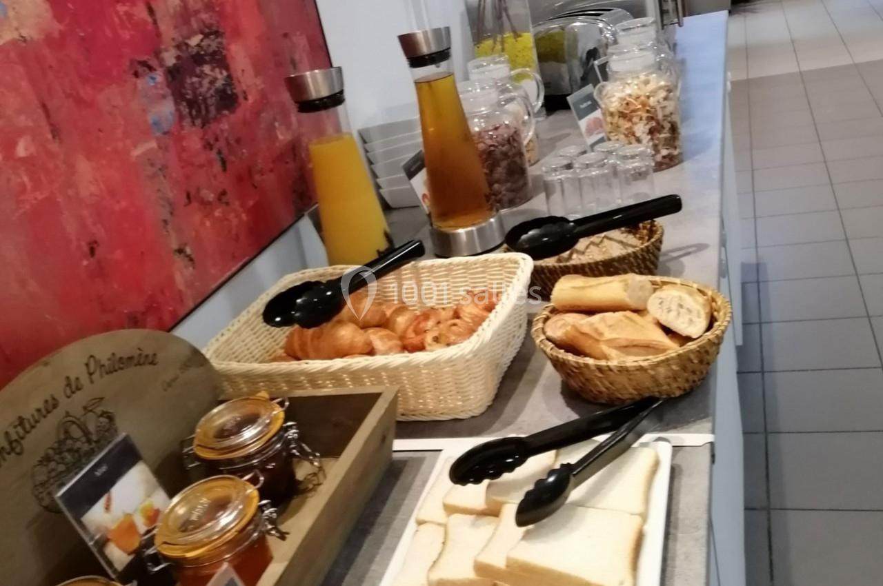 Buffet de petit-déjeuner avec viennoiseries, pain, confitures, jus de fruits et céréales disposés sur une table.