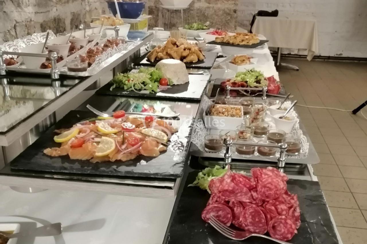 Buffet varié avec charcuterie, poissons, salades, plats chauds et desserts disposés sur des plateaux en ardoise.