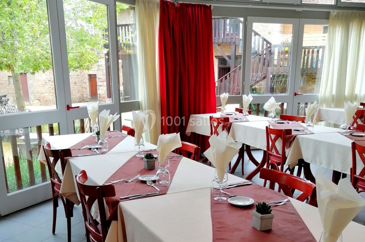 Salle de restaurant lumineuse avec nappes blanches et rouges, tables dressées et grandes fenêtres donnant sur l'extérieur.