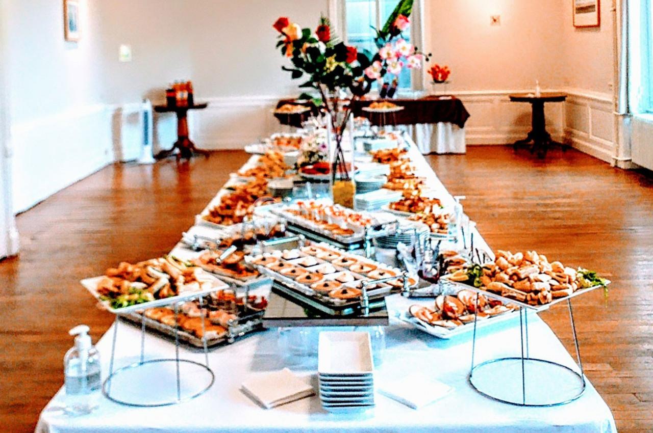 Table garnie d'un buffet varié avec des plats salés et sucrés, dans une salle lumineuse au parquet en bois.
