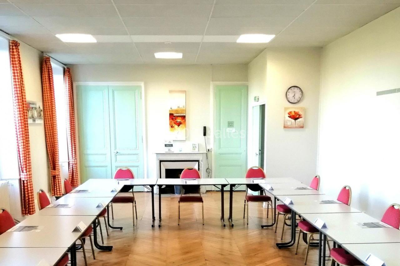 Salle de réunion lumineuse avec tables disposées en U, chaises rouges et décoration murale colorée.